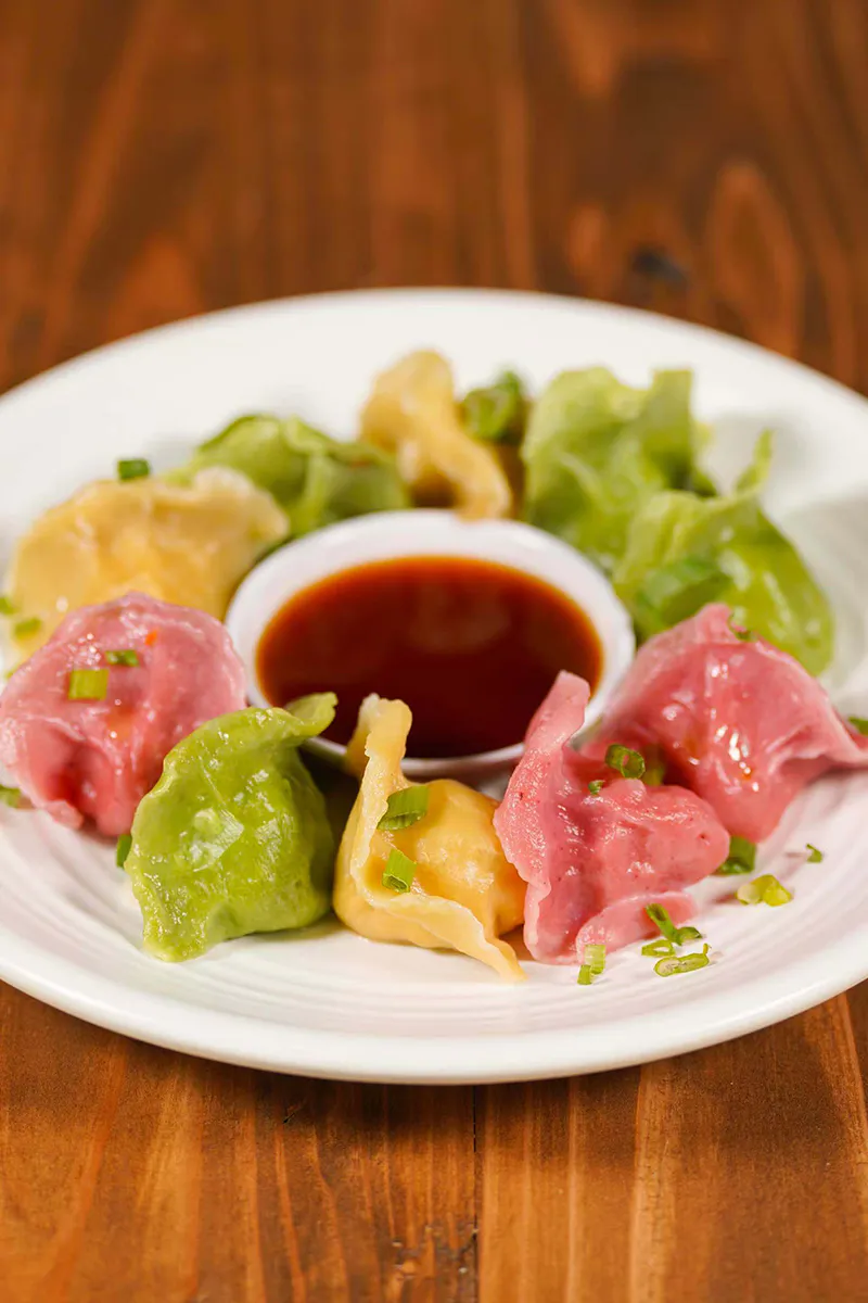 Assorted colorful vegetable dumplings arranged on plate with side soy dipping sauce at One More Bite Dumpling, a Chinese Restaurant in Yucaipa