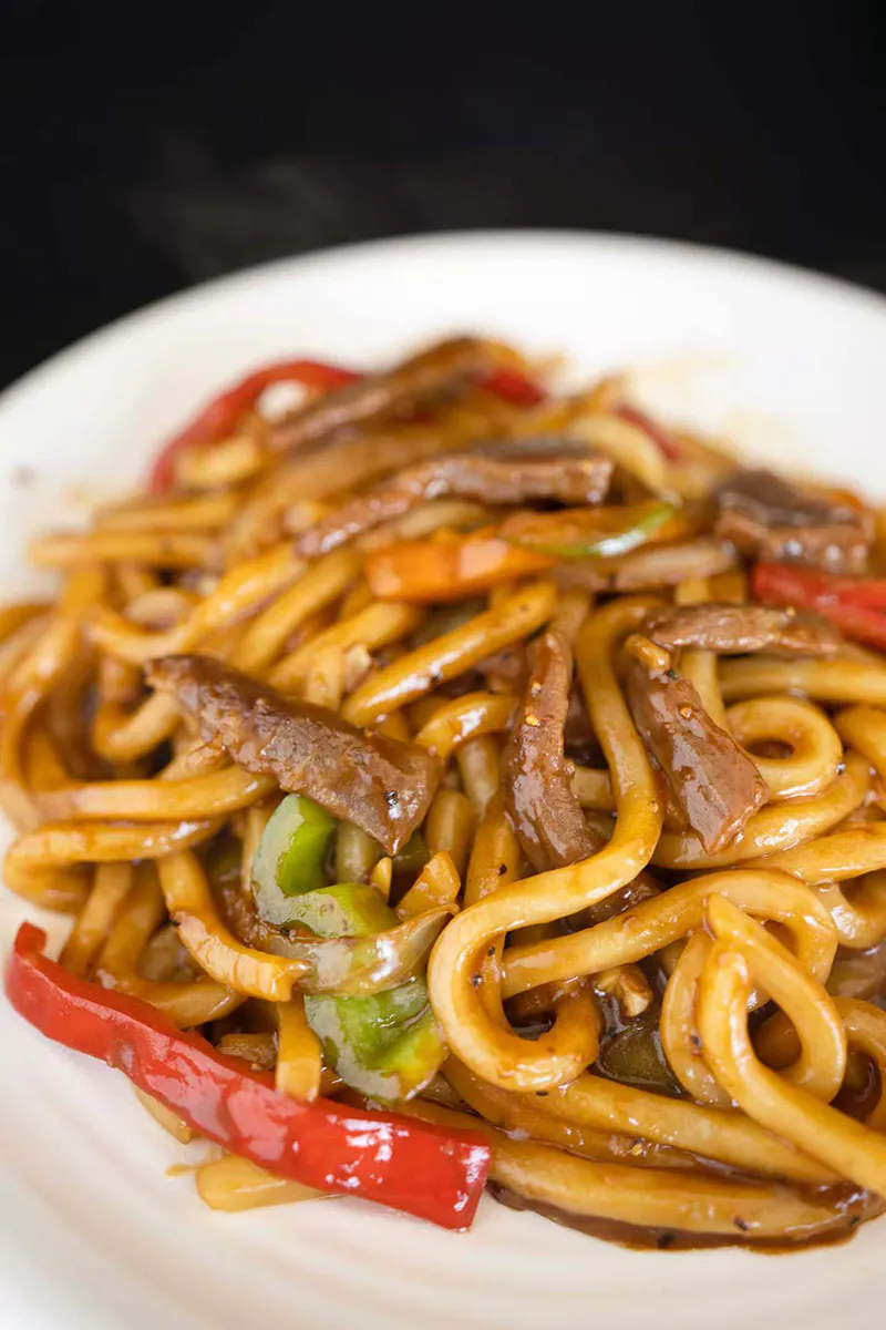Beef udon stir fry mixed with bell pepper strips and glossy dark sauce at One More Bite Dumpling, a Chinese Restaurant in Yucaipa