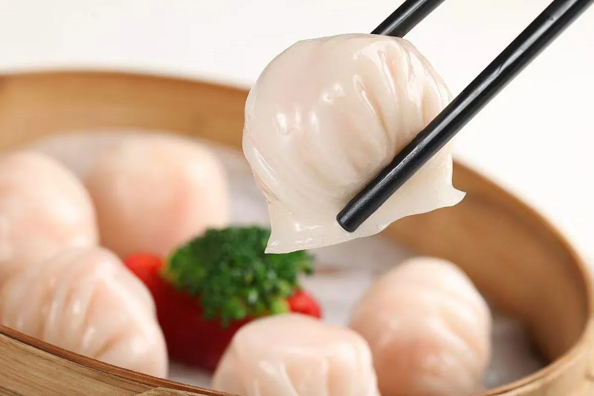 Shrimp har gow dumpling held by chopsticks above bamboo steamer basket at One More Bite Dumpling, a Chinese Restaurant in Yucaipa