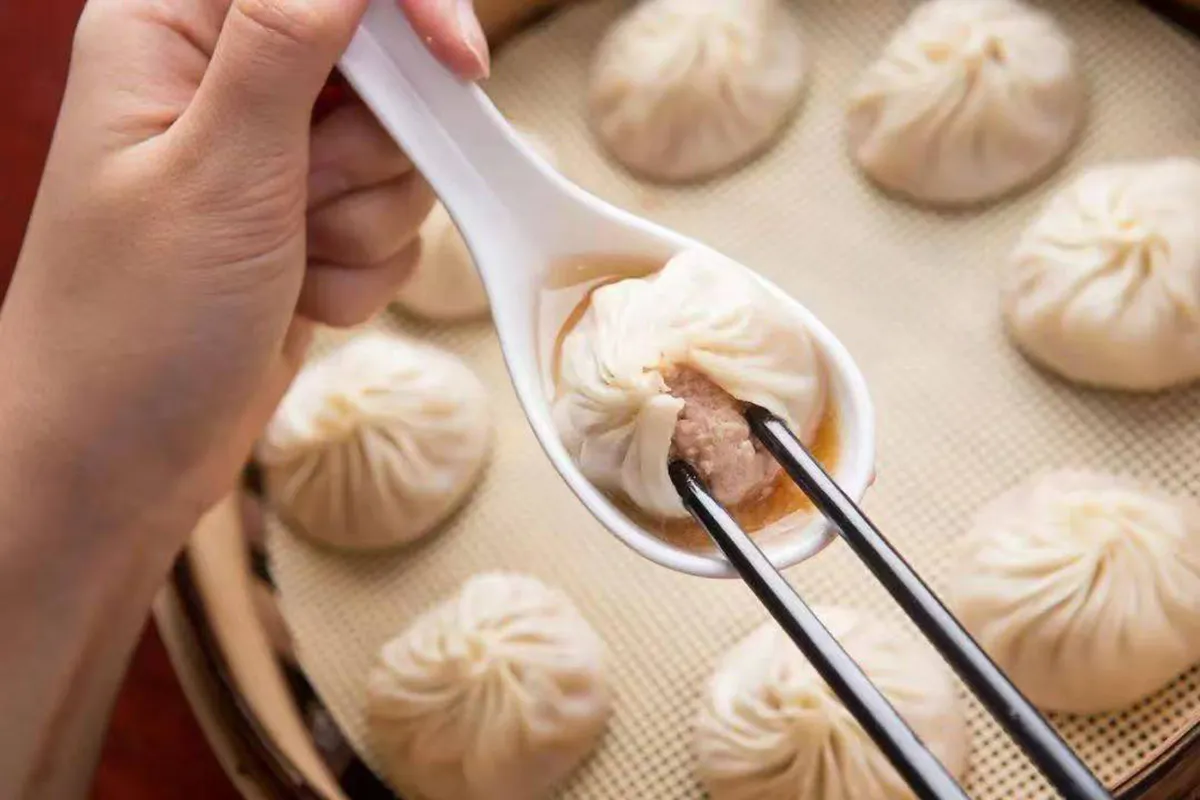 Soup dumpling held on a white spoon with chopsticks above bamboo steamer baskets at One More Bite Dumpling, a Chinese Restaurant in Yucaipa