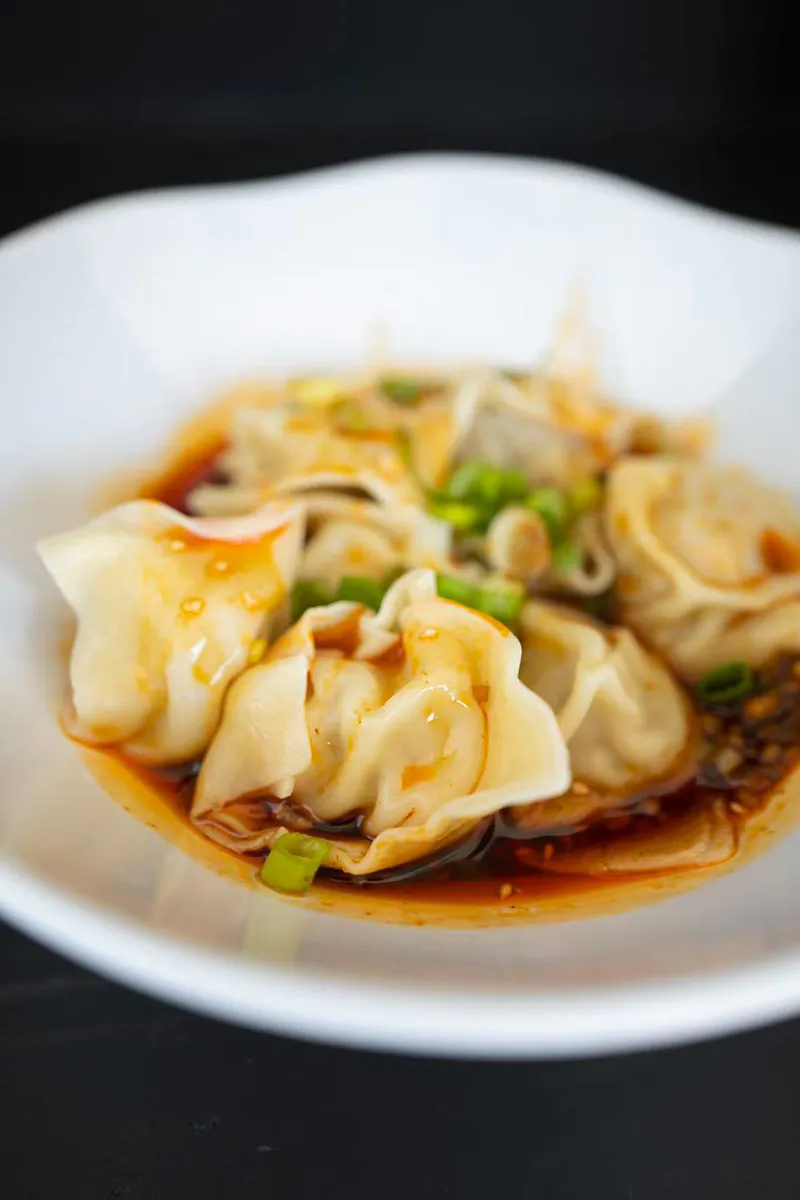 Spicy boiled dumplings served in red chili sauce topped with chopped green onions at One More Bite Dumpling, a Chinese Restaurant in Yucaipa