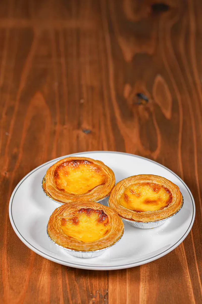 Three baked egg tarts with flaky pastry crust on simple white plate at One More Bite Dumpling, a Chinese Restaurant in Yucaipa