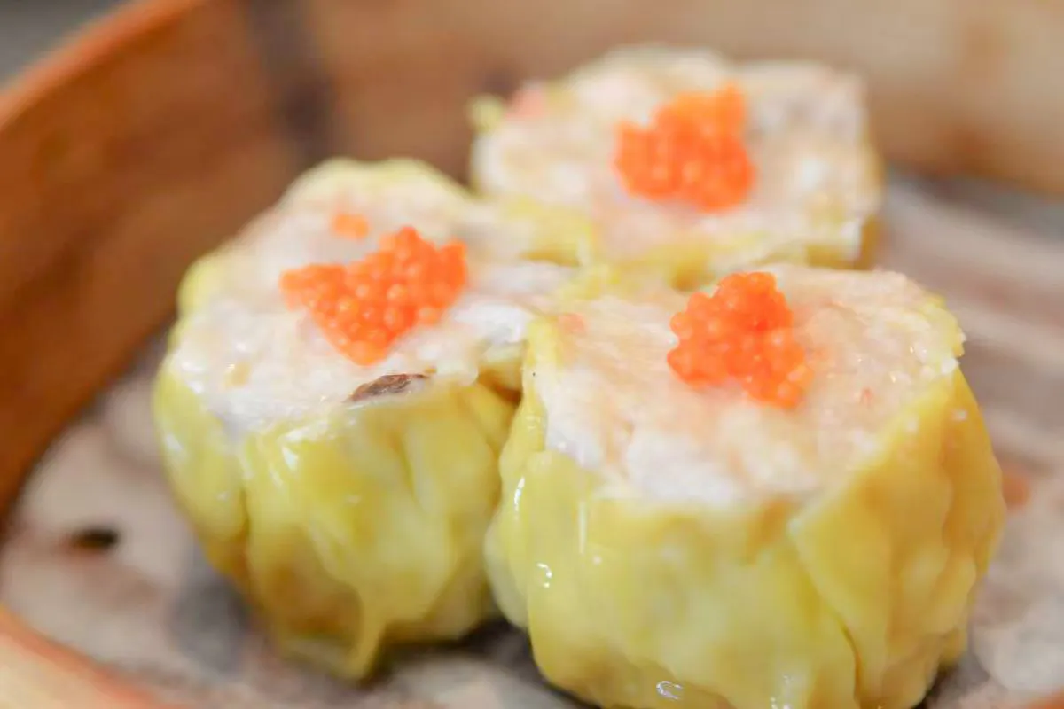 Three siu mai dumplings topped with orange fish roe inside a bamboo steamer at One More Bite Dumpling, a Chinese Restaurant in Yucaipa